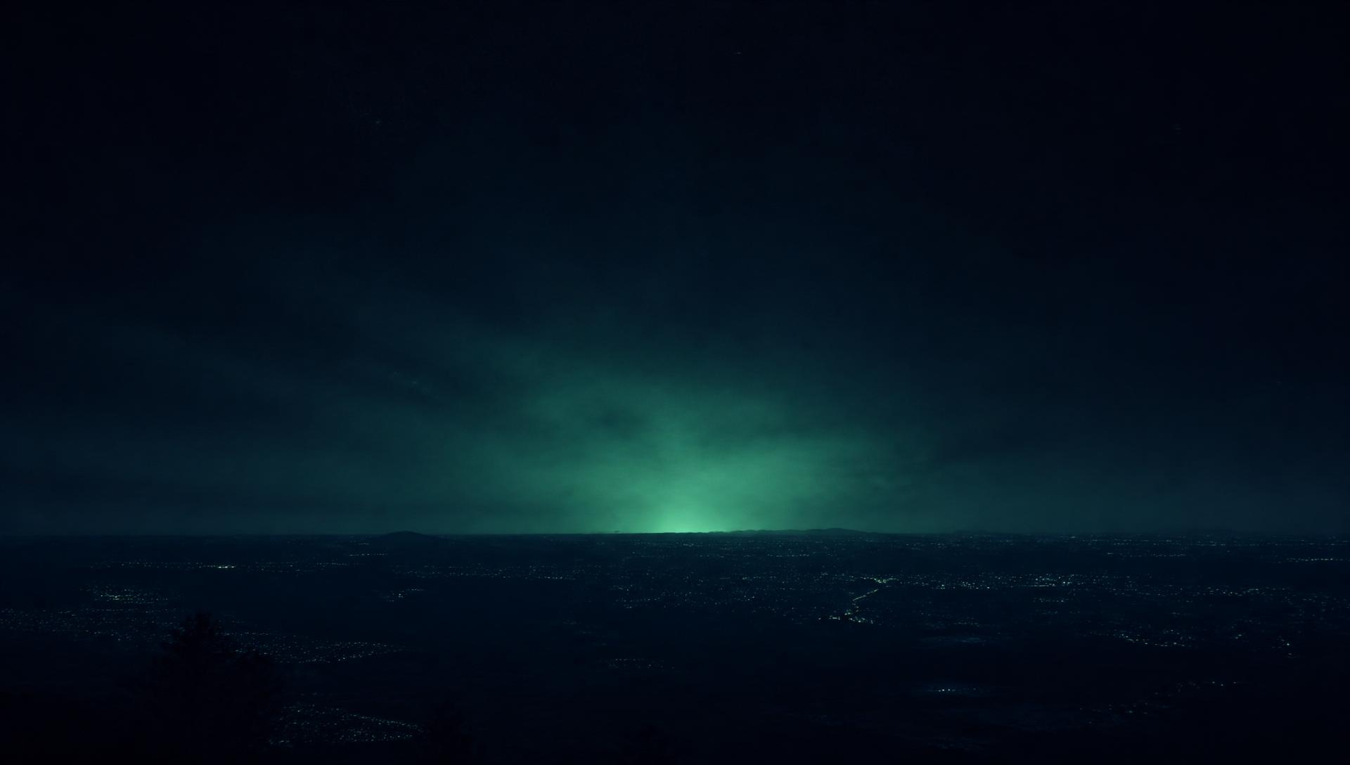 A dark night horizon seen from above with a faint green glow on the skyline